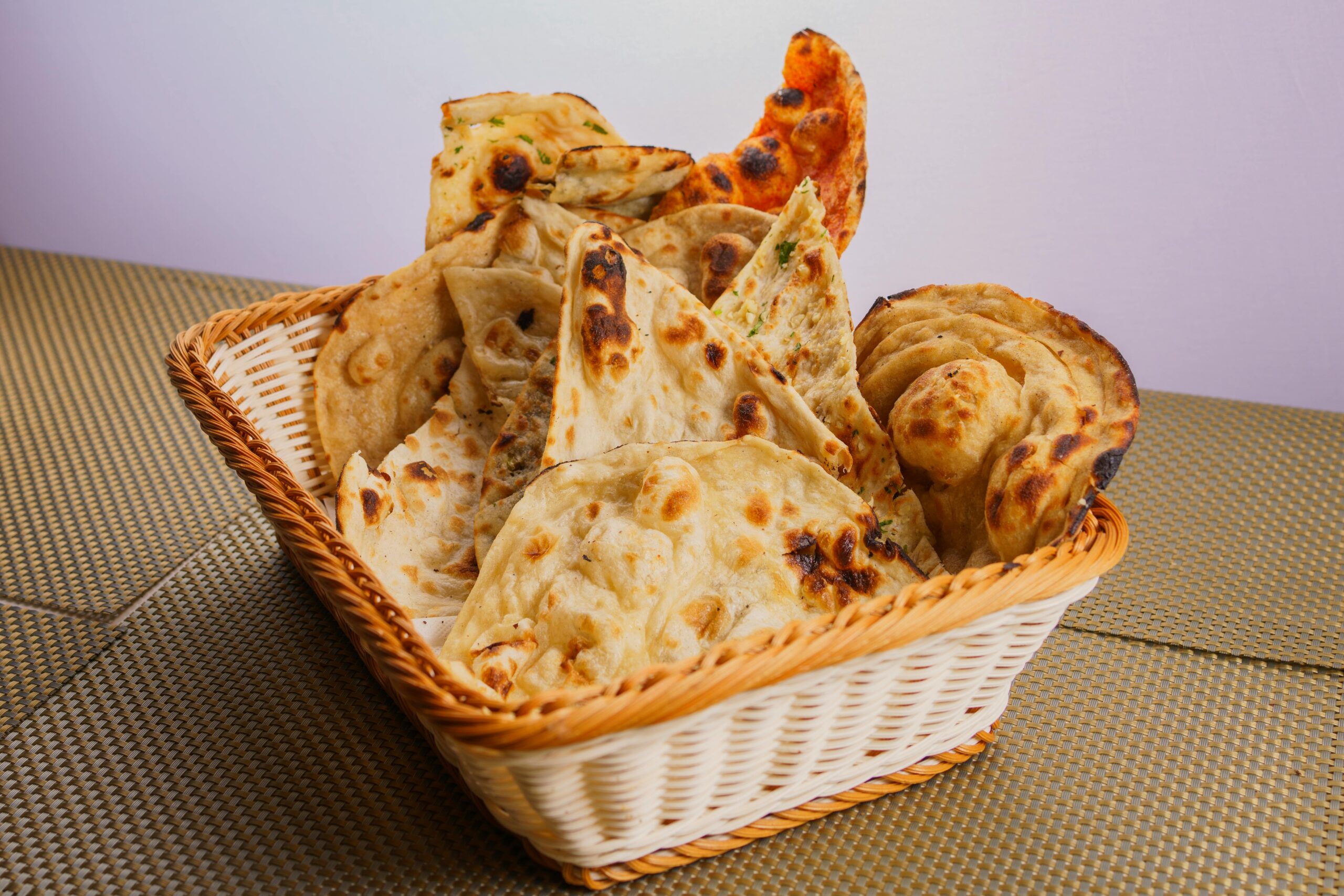 A variety of traditional Indian breads like naan and roti in a wicker basket, perfect for a delicious meal.